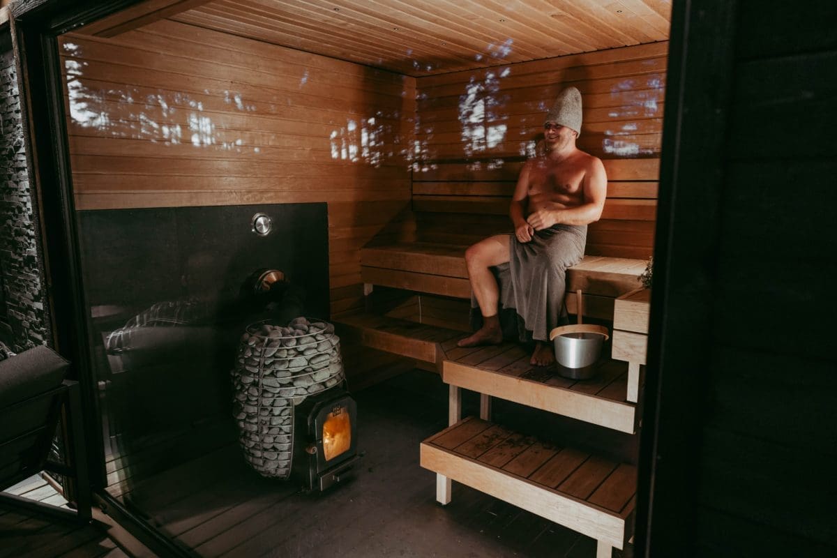 Man relaxing in a wooden sauna heated by a HUUM HIVE Wood sauna heater, embodying modern design and ancient sauna-building wisdom
