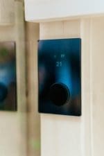 black glass huum uku wifi controller thermostat on light wood wall outside a modern sauna.