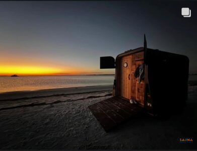 Mobile Sauna Trailer At Sunset On A Beach With Ramp Door Open And Cedar Entry Glowing.